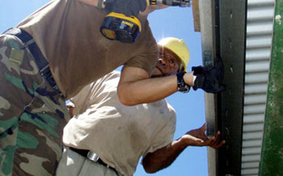 Petty Officer 3rd Class Johnathan Myrick, a builder assigned to U.S. Naval Mobile Construction Battalion 133, works with a Papua New Guinea Defense Force Engineering Battalion member to attach a water catchment system at the Popondetta Secondary School.