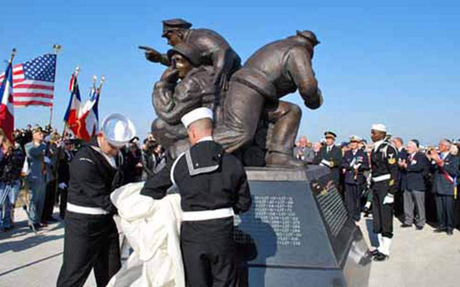 French and American officials and spectators including D-Day vets applaud as a memprial to the U.S. Navy participation in D-Day invasion is unveiled on Saturday at Utah Beach in Normandy, France.