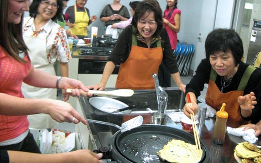 Krystal Roebuck, chairman of Okinawa Enlisted Spouse Club at Kadena Air Base, left, gets a helping hand Saturday from Sachiko Yamada, right, in flipping over an Okonomiyaki pancake on the hot plate. A cooking exchange wass part of the Bilateral Friendship Day at Kadena Town, Okinawa.