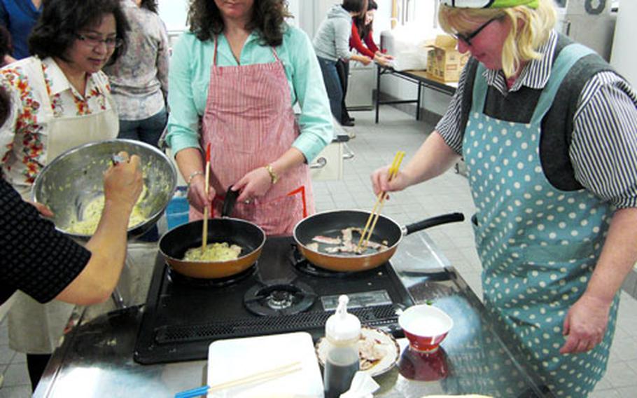 Toyoko Genka of Kadena Town, front left, oversees her American counterparts, Katherine Perce, center, and Christina Israel, both of the Kadena Officers&#39; Spouse Club, as they work with their chopsticks to make Okonomiyaki pancakes.