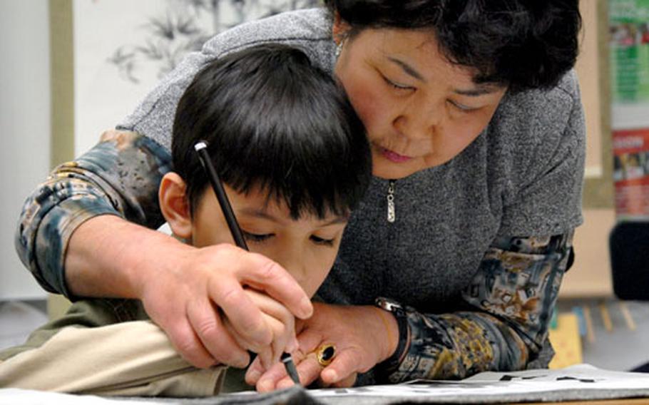 Volunteer Eiko Takada helps 6-year-old Liam Sater finish a Japanese calligraphy project during the Japan Day event.