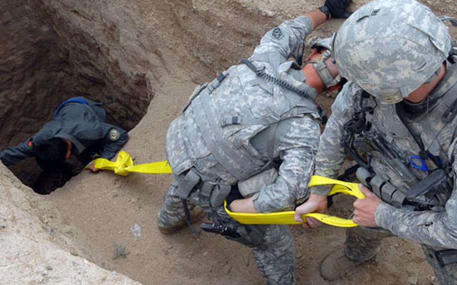 Spc. Joshua Harmon, right, and Sgt. Gino Darrough hold a tow cable while a National Police officer descends into a well to check for hidden weapons near Khaneh Gerdab, Afghanistan.