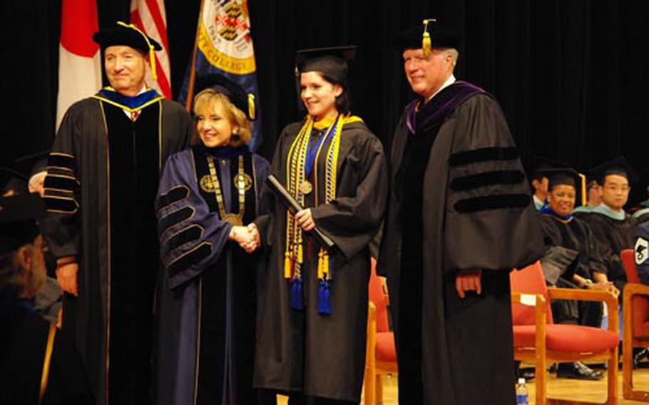 A new graduate receives her diploma and Summa cum laude honors from William C. Beck II, left, vice president and director of University of Maryland University College Asia; Susan C. Aldridge, second from left, president of University of Maryland University College; and William Wood, right, of the Board of Visitors, University of Maryland University College.