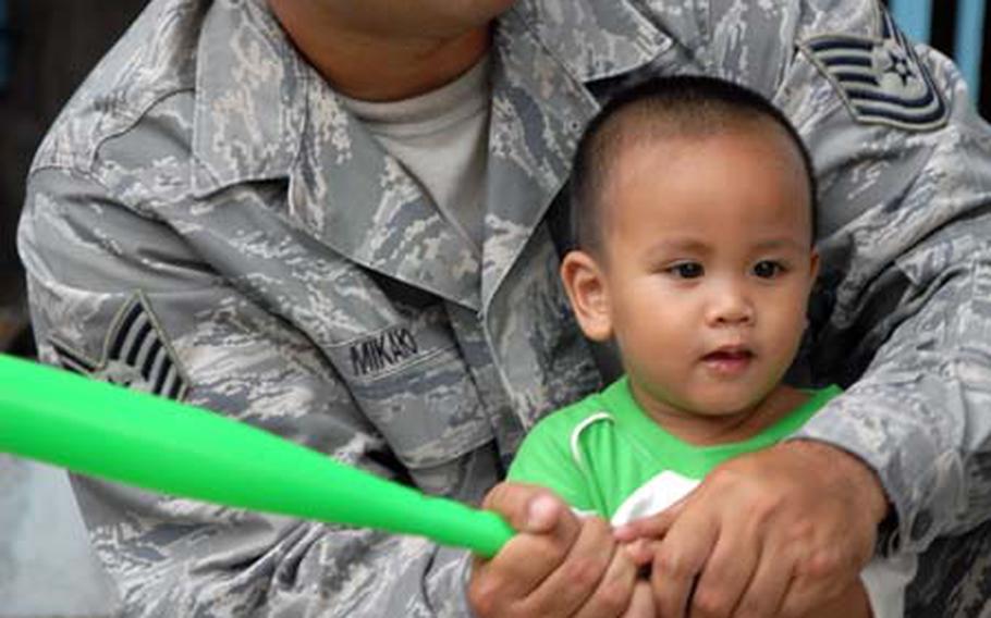 Tech. Sgt. Jeff Mikaio, of the 56th Fighter Wing at Luke Air Force Base, Ariz., teaches toddler Alex how to play baseball during a visit to the Duyan Ni Maria Children’s Home in Angeles City, Philippines, on Friday.