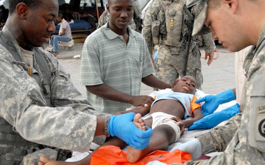 Sgt. Willie Green, left, elevates the broken leg of an 8-year-old boy after he and other patients were moved out of the hospital buildings after the earthquake hit Port-au-prince Wednesday morning. Pfc. Anthony Invzitari, right, helps.