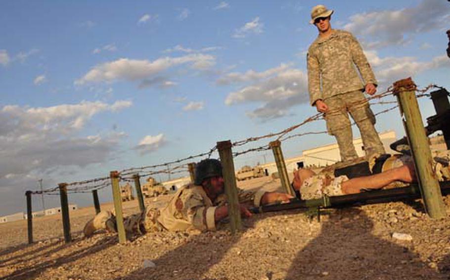 Sgt. William Winstead watches Iraqi soldiers crawl under barbed wire while hauling a soldier playing an injury victim on a litter. The Iraqi soldiers were participating in a timed obstacle course as part of their training in combat first aid.
