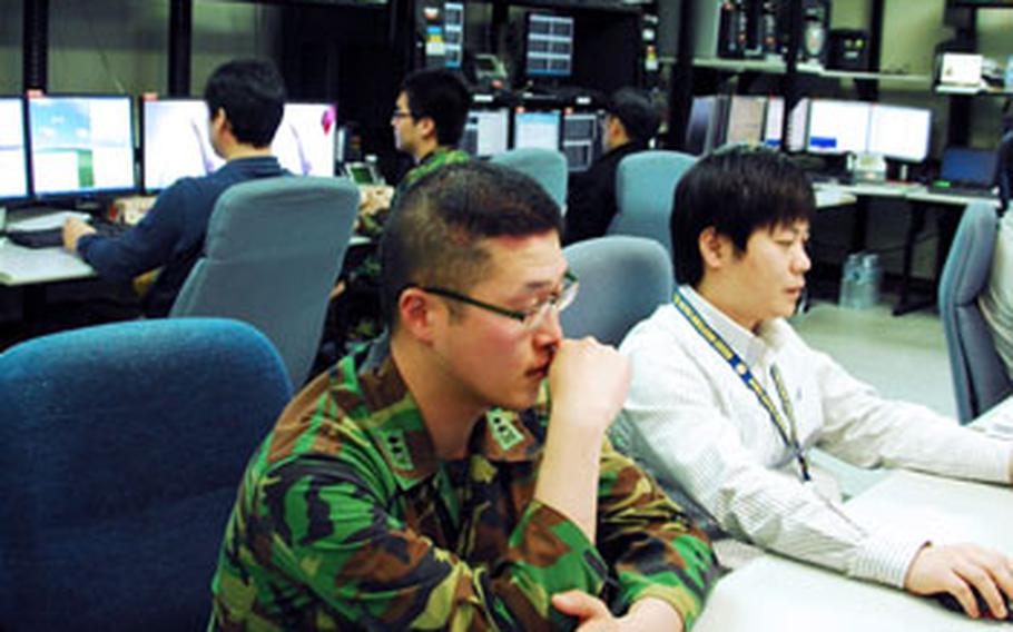 Workers sit inside the technical control room of the Korea Battle Simulation Center&#39;s Walker Center, on U.S. Army Garrison-Yongsan. Behind them is a video teleconferencing screen with links to other bases in South Korea and the United States. Bases in both countries participate in the annual Key Resolve exercise, which includes computer-simulated battle situations.
