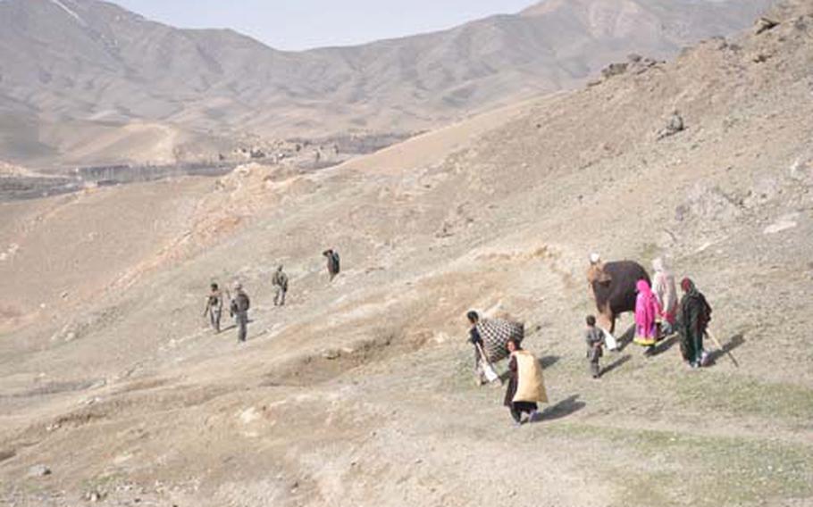 Villagers walk by a patrol of U.S. and Afghan soldiers in the hills above Wardak province’s Tangi Valley.
