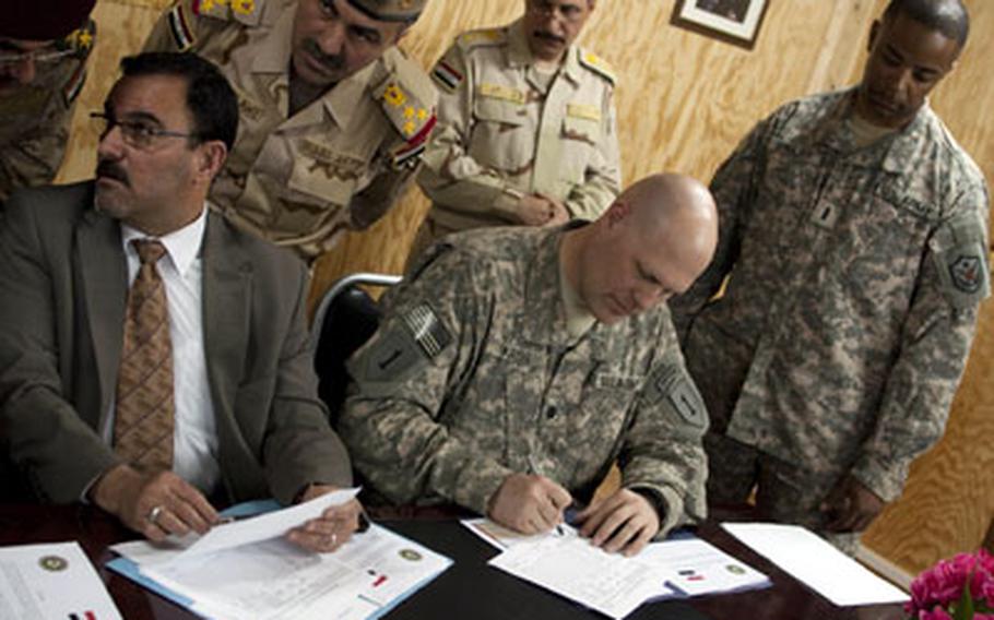 U.S. Army Lt. Col. Paul Kreis, center, and Samir al-Haddad, an official from the office of the Iraqi prime minister, sign papers transferring Forward Operating Base Summerall from U.S. to Iraqi control. Iraqi Army Brig. Gen. Abdullah al-Dulawe, third from left, and U.S. Army Chief Warrant Officer Kenneth Shuler, right, look on.