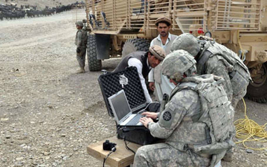 Soldiers from a route clearance unit enroll passers-by in a database system after setting up a checkpoint along Route Alaska.