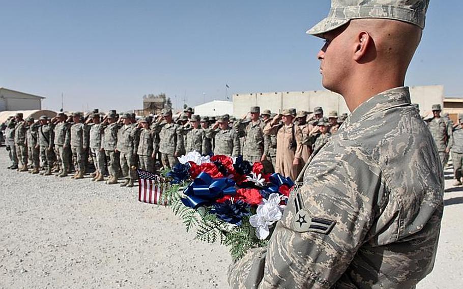 As other troops salute in the background, an airman holds a wreath to be laid Monday during a Memorial Day ceremony at Kandahar Airfield. The small ceremony, honoring fallen troops during the nation&#39;s wars, was attended by about 100 people at Camp Samek, heaquarters of the 451st Expeditionary Air Wing.