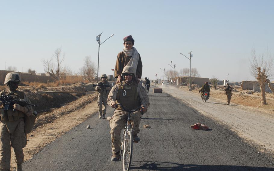 An Afghan translator working for the Marines takes a local boy for a bike ride on the boy's bike on Marjah's main drag. The road had just been paved, a first in the town.