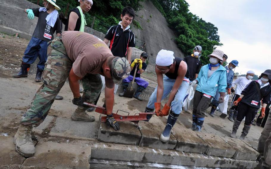 Petty Officer 1st Class Joshua Thonnissen, left, and a Japanese volunteer replace a heavy, brick drainage ditch cover while cleaning up tsunami damage Thursday in Miyako, Japan.