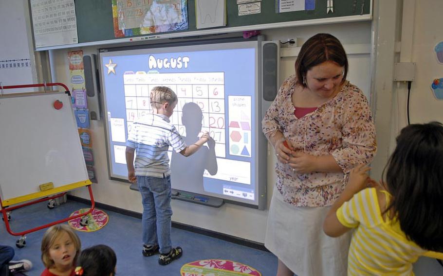 Second-grader Jameson Muse writes a calendar date on a Smart Board, while teacher Holly Magcalas helps another student on the first day of school Monday at Vogelweh Elementary School in Kaiserslautern, Germany.