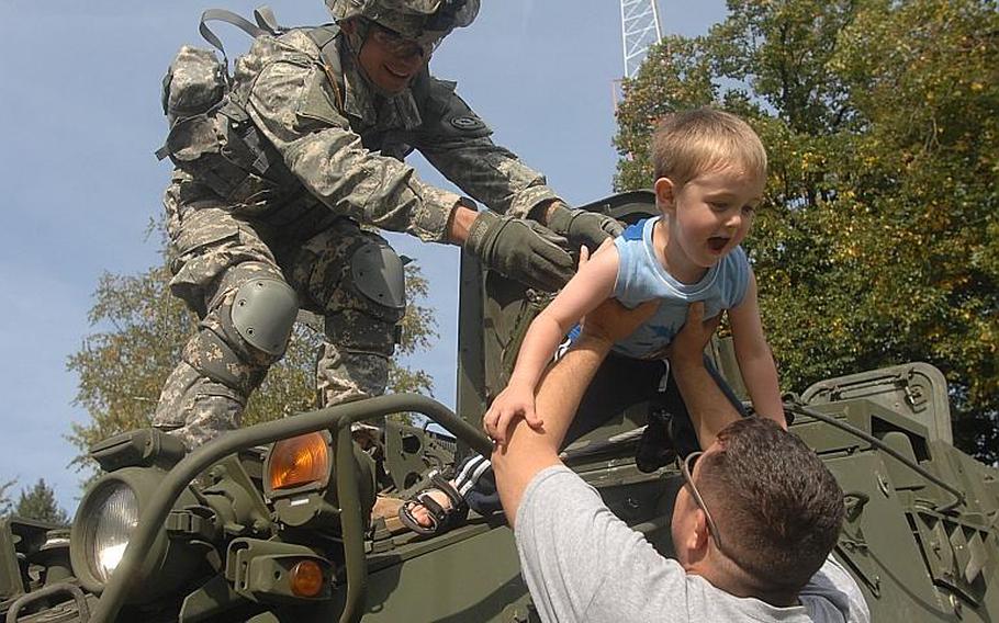 A soldier with the 2nd Stryker Cavalry Regiment hoists 4-year-old Wyatt Moore from the top of a Stryker down to the arms of his father, Sgt. Matthew Moore, 33, of the Regimental Support Squadron before Sunday's 9/11 memorial ceremony at Rose Barracks in Vilseck.