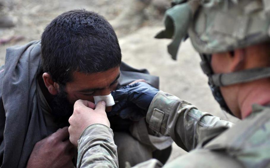 Cpl. Evan Jenkins, 3rd Platoon, Destroyer Company, 2nd Battalion of the 87th Infantry Regiment, bandages the nose of a man who was lightly injured during a night raid. The man had been on his way to open the door when soldiers, after knocking several times, kicked it in.