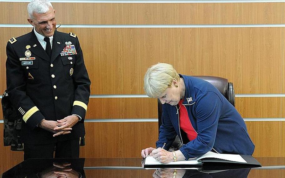 As U.S. Army Europe commander Lt. Gen. Mark Hertling watches, Joan Shalikashvili, widow of the former Chairman of the Joint Chiefs of Staff Gen. John Shalikashvili, signs the guest book on a desk used by her husband. Earlier Thursday, they had dedicated the new U. S. Army Europe mission command center in Wiesbaden, Germany, to the late general.
