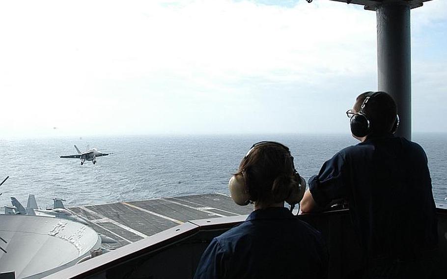 A fighter jet approaches the deck of the USS George Washington on Sunday as a couple of crewmembers look on. The George Washington has been in the waters around South Korea participating in separate exercises with the navies of Japan and the South.