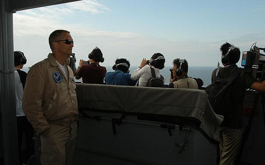 Capt. David A. Lausman, left, commander of the USS George Washington, takes in the action during Sunday&#39;s exercise with the South Korean navy in the Yellow Sea. Behind him, members of the media monitor fighter jet takeoffs and landings.