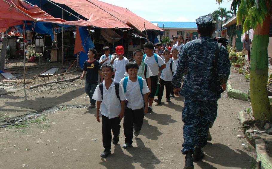 A sailor and Filipino school children pass the Alvarez Tent City, the Philippines, in July 2014. Typhoon evacuees were living there and some still occupy classrooms at the childrens' school, more than seven months after the devastating storm hit the islands.