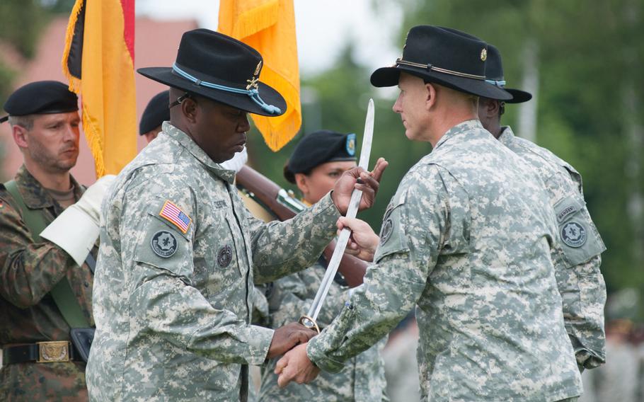 The outgoing 2nd Cavalry Regiment commander, Col. Douglas Sims, hands the ceremonial noncommissioned officer sword to interim command Sgt. Maj. Martin Celestine during a mass change of command ceremony held at Vilseck, Germany, Tuesday, July 15, 2014.