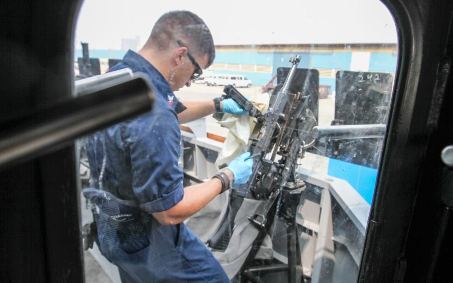 A sailor aboard the USS Monsoon cleans a machine gun placed outside the ship's bridge, Aug 28, 2014. The Monsoon is outfitted with .50 cals, the lightweight Griffin Missile System and a 25mm autocannon.