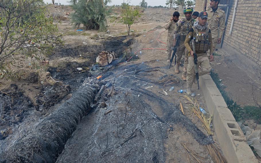 Iraqi soldiers walk past a smoldering palm tree destroyed in a morning mortar attack March 12, 2015, in Karmah, Iraq. The soldiers at this front near Fallujah face snipers and scattered improvised explosive devices.