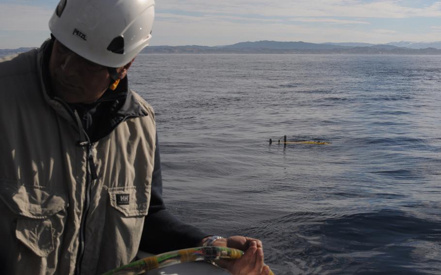 A crew member of the NATO research vessel NRV Alliance feeds a hydrophone cable into the water during the deployment of an autonomous underwater vehicle (pictured in the water). The hydrophone is a listening device that trails behind the AUV to pick up echoes from sound waves projected into the water by the Alliance. The ship and its detachment of scientists from NATO's Centre for Maritime Research and Experimentation in Italy are testing several AUVs in the North Sea off the coast of Norway as part of an anti-submarine warfare exercise called Dynamic Mongoose.