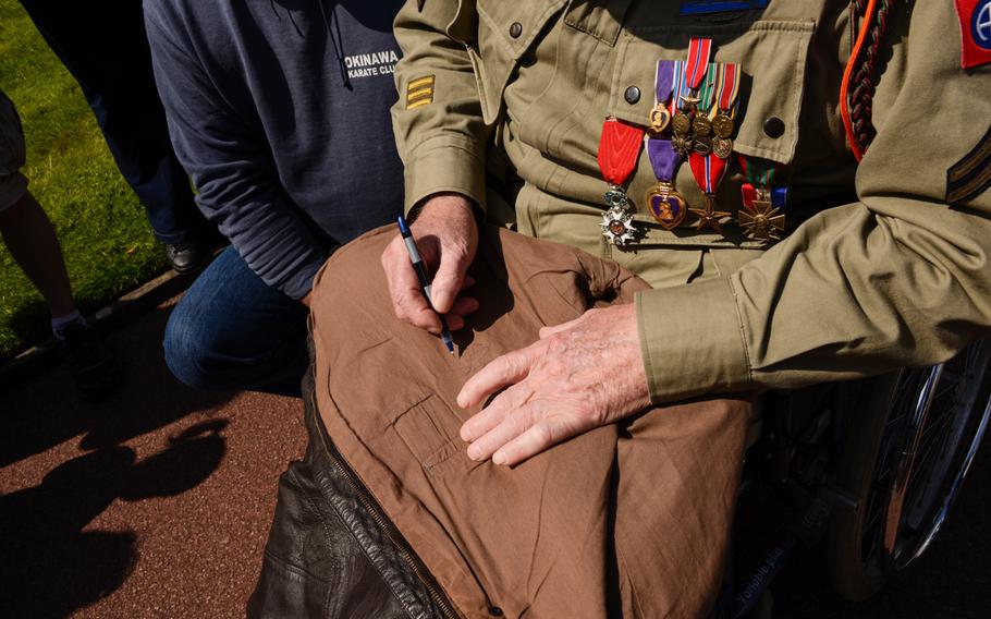George Shenkle, 93, signs an autograph after the Memorial Day ceremony at the Normandy American Cemetery, Sunday, May 24, 2015. Shenkle, a member of the 82nd Airborne Division, jumped into Normandy on D-Day as well as Operation Market Garden before later being wounded in the Ardennes during the Battle of the Bulge.