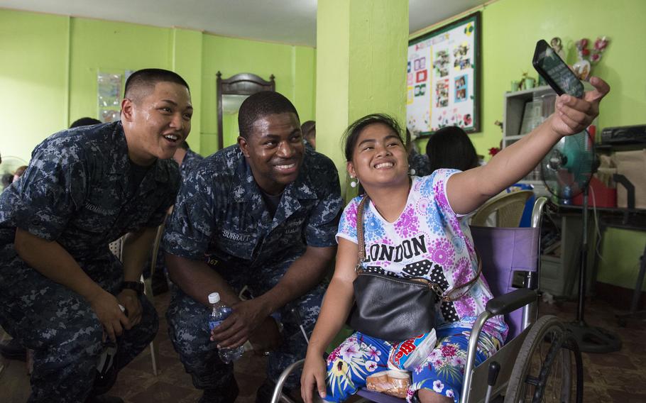 Fireman Xavier Phommavong and Petty Officer st Class Broderick Surratt, both assigned to the USS Shiloh pose for a selfie with a student from the Association of Differently Abled Persons school during a community relations project in Olongapo City, Philippines.