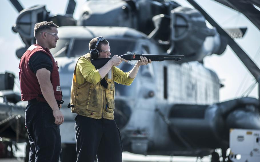 Petty Officer 3rd Class Timothy Tennant, right, fires an M-500 12-gauge shotgun during a weapons qualification exercise on the flight deck of the USS Essex as it sails in the Pacific Ocean on June 3, 2015.