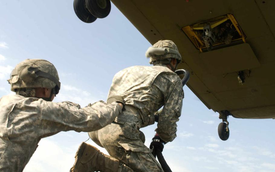 Two New York Army National Guard Soldiers from the 427th Brigade Support Battalion prepare to attach a sling load hook to a CH-47 Chinook helicopter July 19, 2015, at Fort Drum, N.Y.