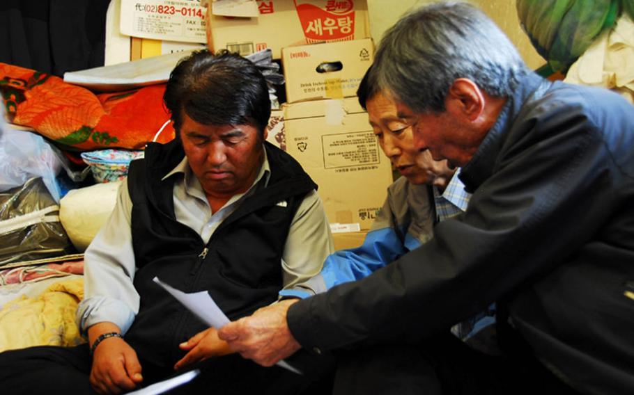 Jeong Ji-eun, from left to right, Jang Seok Ju and Jon Chon-bong look at old aerial photographs in 2011 of Wolmi Island, where they lived before the U.S. bombed the island in September 1950 to rid it of North Korean troops. The men were part of a group of approximately 160 former residents of Wolmi Island that filed suit against the government, seeking compensation for property lost during the bombing.