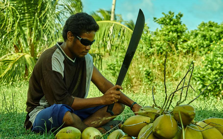 A man from the chief's village on Fais Island breaks open coconuts with a machete while he waits for word of the U.S. Air Force's expected arrival for Operation Christmas Drop on Dec. 8, 2015. He and other island men will be expected to help carry the 800 pounds' worth of humanitarian aid and Christmas presents from an open field in the jungle and walk the two boxes about 20 minutes away to the men's house in the main village.
