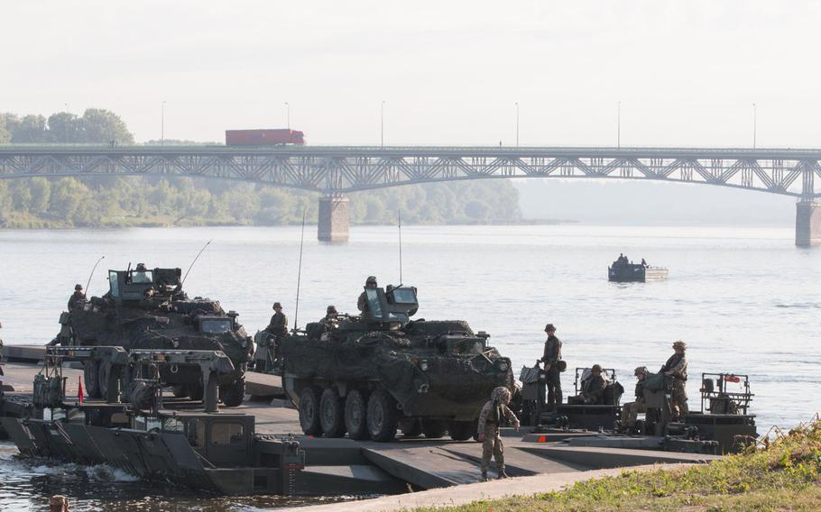 As morning traffic continues across the bridge behind them, U.S. Army Strykers belonging to the 2nd Cavalry Regiment cross the Vistula River in Chelmno, Poland, on Wednesday, June 8, 2016.
