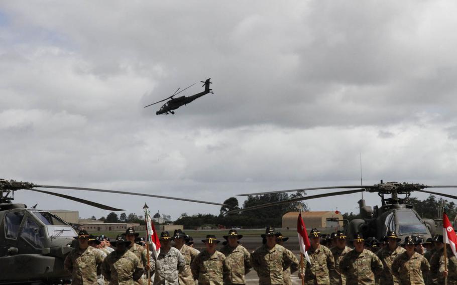 Members of the 6th Cavalry Regiment, 25th Combat Aviation Brigade, assemble near the flight line at Wheeler Army Airfield, Hawaii, as an Apache helicopter demonstrates some of its maneuvering capabilities during a ceremony, Thursday, June 9, 2016.