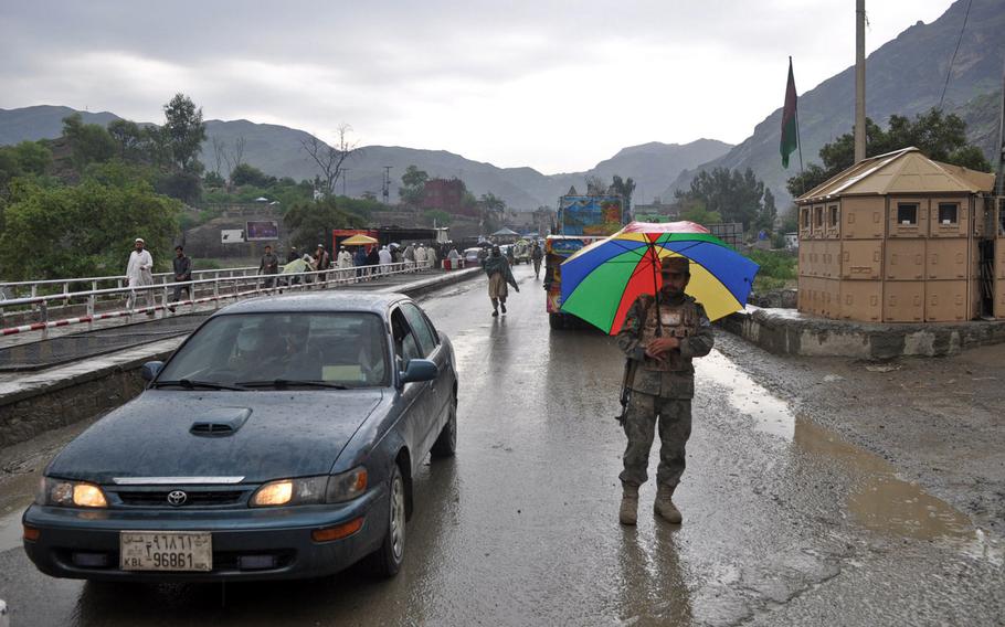 An Afghan Border Police officer shelters himself from the rain while guiding traffic at Torkham Gate, Afghanistan's busiest border crossing. Pakistani and Afghan forces exchanged fire on Sunday, June 12, 2016, over construction on the Pakistani side of the border.