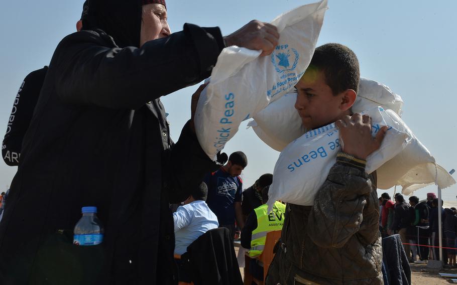 A woman loads a bag of chick peas, part of a monthly family food ration, onto the shoulders of a young helper at the Khazir displacement camp about 20 miles east of Mosul, Iraq, on Monday, Nov. 7, 2016. Roughly 1,300 families forced to flee fighting in and around Mosul have settled into the camp in recent weeks.