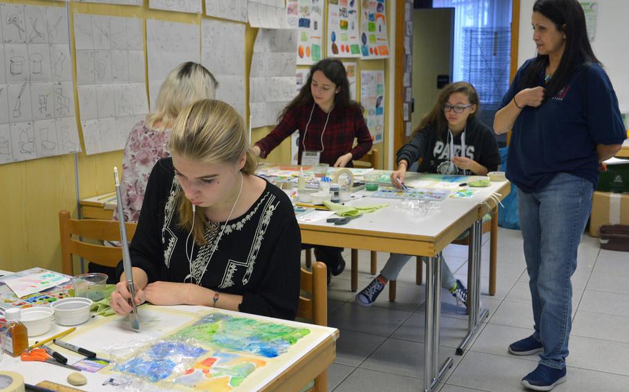 Watercolor instructor Najet Ayachi, right, looks over her artists' works during a session at Creative Connections, an annual weeklong DODEA-Europe performing and visual arts symposium for high school students.