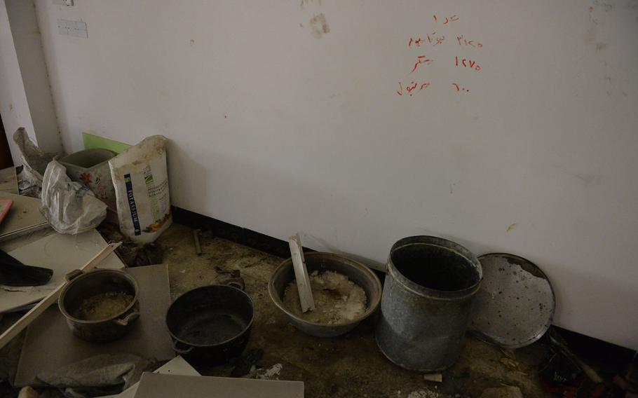 A recipe for rocket propellant is scrawled on the wall of a church building in Qaraqosh, Iraq, behind an array of metal pots and tubs Islamic State munitions makers likely used to mix the formula, Dec. 17, 2016.