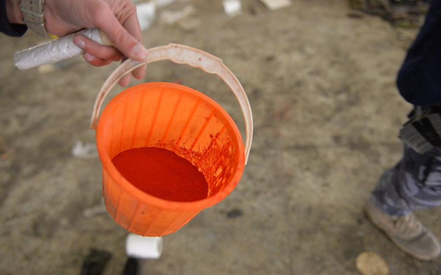 A police officer holds a tub filled with red powder, possibly iron oxide, found inside a building on the grounds of St. George's Church in Qaraqosh, Iraq, Dec. 17, 2016. The compound may have been used in making rocket propellant in the building.