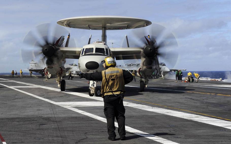 A sailor directs an E-2D Hawkeye assigned to the Tigertails of Airborne Early Warning Squadron 125 across the flight deck of the USS Theodore Roosevelt in 2015.
