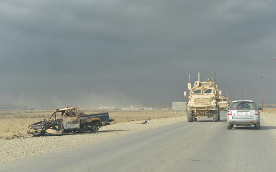 A convoy of Mine Resistant Ambush Protected vehicles passes a burned-out truck on a road near Qayara, Iraq, on Nov. 10, 2016.