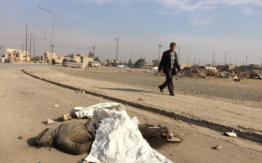 A pedestrian passes the body of a person locals said was an Islamic State fighter, near Mosul University on Saturday, Jan. 21, 2017. 