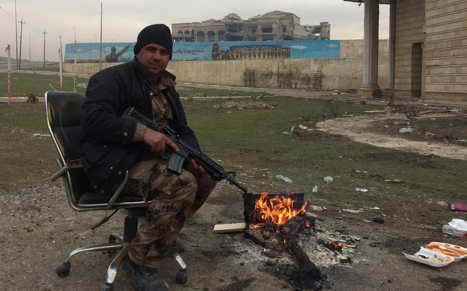 An Iraqi soldier keeps warm in front of a palace in Mosul, Iraq, on Wednesday, Jan. 25, 2017. The mural behind him depicts the Islamic State group's dream of the conquest of Rome.