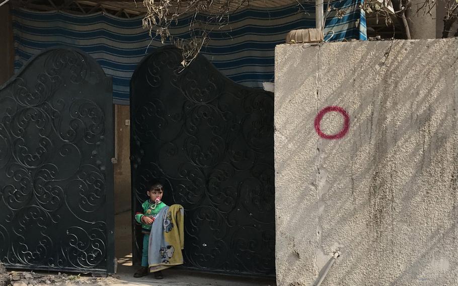 A child stands in front of a driveway gate at a home in the al-Dandan neighborhood of Mosul on Wednesday, March 8, 2017. The red circle on the wall marked the house as having a covered driveway suitable for concealing an Islamic State car bomb, residents say.