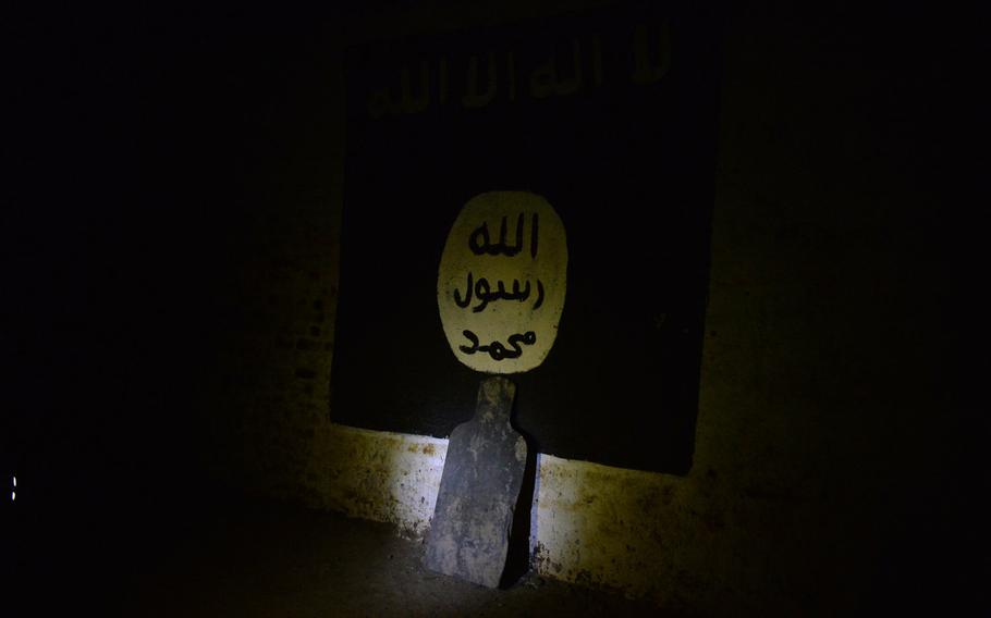 Pictured here on Thursday, March 9, 2017, a marksmanship target leans against a painting of the Islamic State flag on the wall of a railway tunnel that the Islamic State group turned into a covert training base.