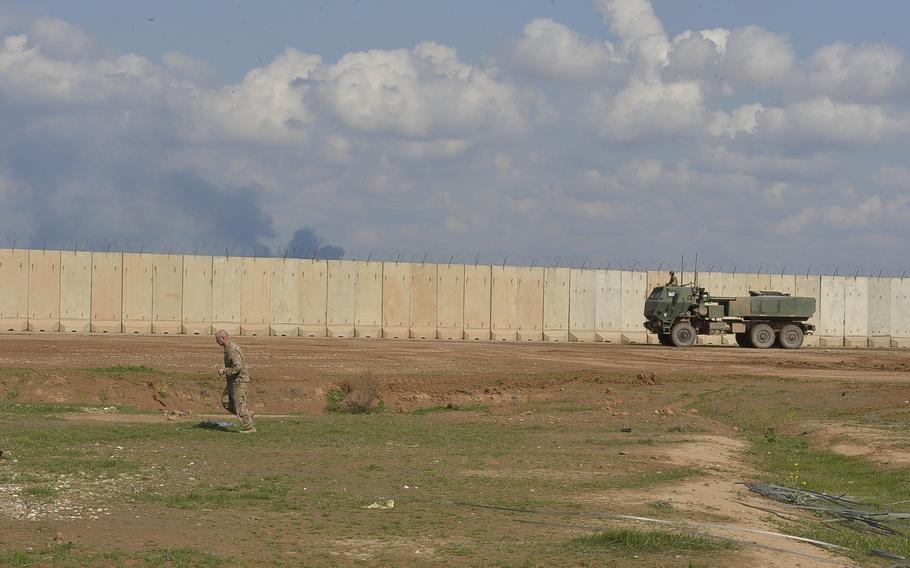 A medium tactical vehicle mounted with a High Mobility Artillery Rocket System and a soldier on foot both rush toward a firing point on Qayara Airfield West, Iraq, after the ''Odin'' battery of the 18th Field Artillery Brigade received a fire mission, March 17, 2017.