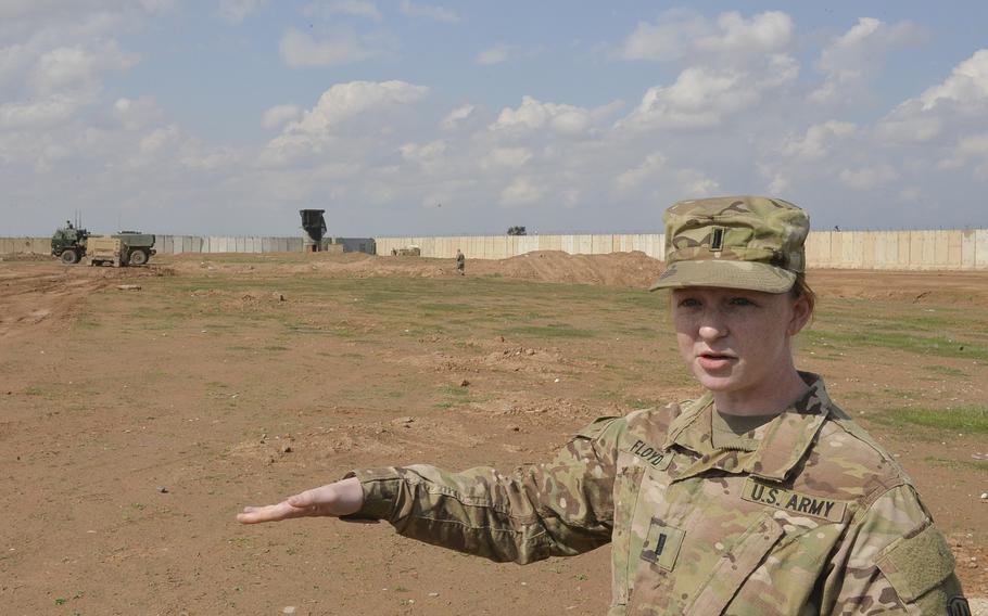 Lt. Mary Floyd, a platoon commander with the ''Odin'' battery of High Mobility Artillery Rocket Systems, explains to reporters how the rocket systems launch their ''smart munitions'' on targets in Mosul, Iraq, during a fire mission at Qayara Airfield West, March 17, 2017. In the background, a truck-mounted HIMARS and a Humvee race to the firing point.