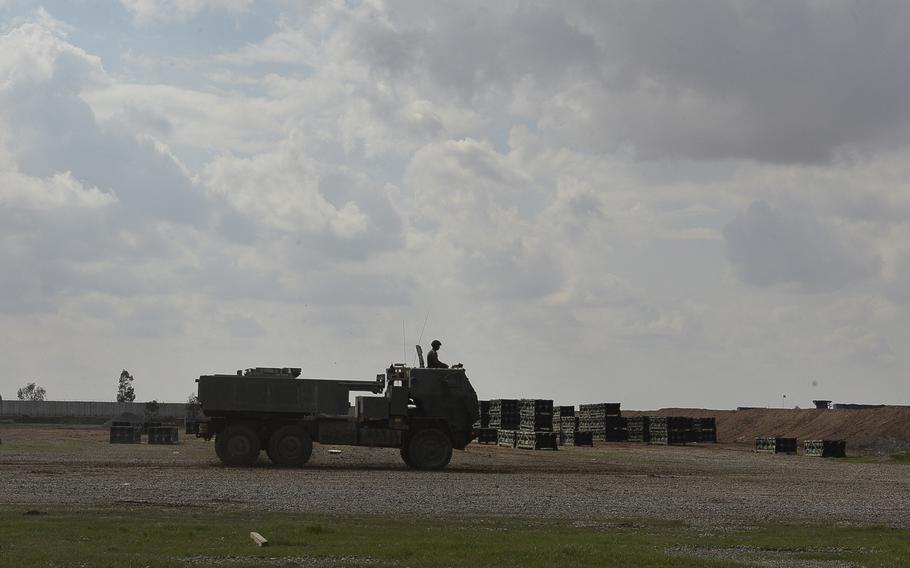 A medium tactical vehicle mounted with a High Mobility Artillery Rocket System drives toward a firing point on Qayara Airfield West, Iraq, past a field full of spent six-pack rocket pods, during a fire mission with the ''Odin'' battery of the 18th Field Artillery Brigade, March 17, 2017.